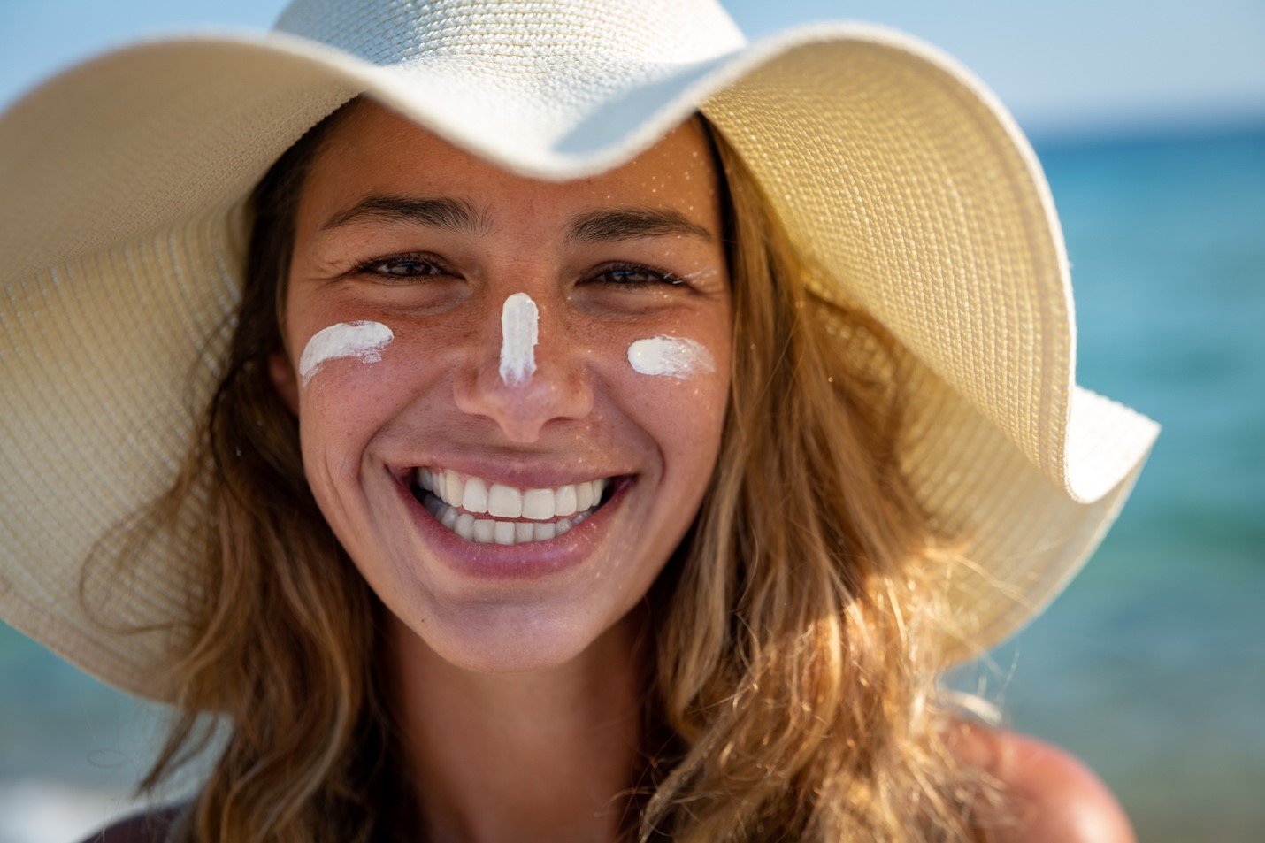 Mulher a sorrir com protetor solar na cara